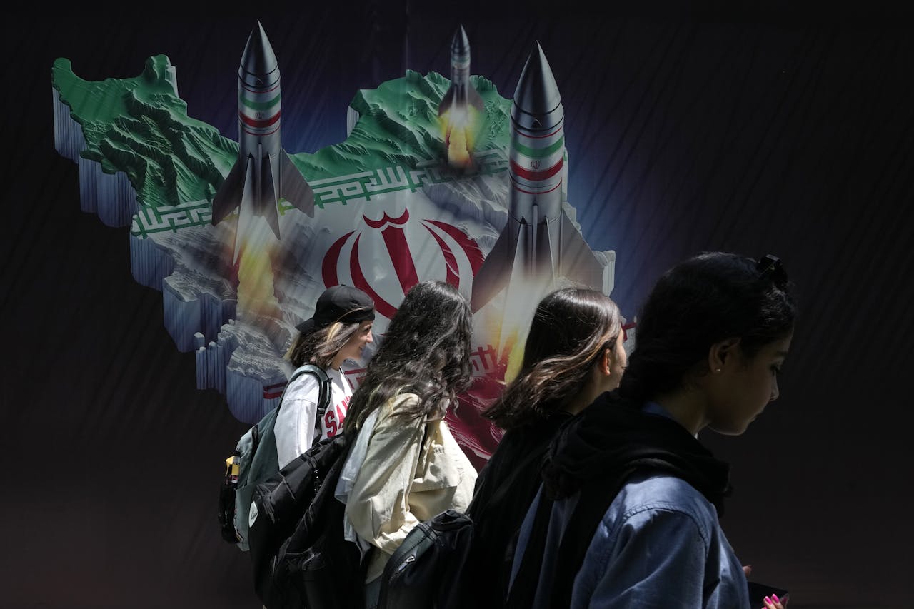 Iraanse vrouwen lopen langs een muurschildering van Iraanse raketten in hoofdstad Teheran.