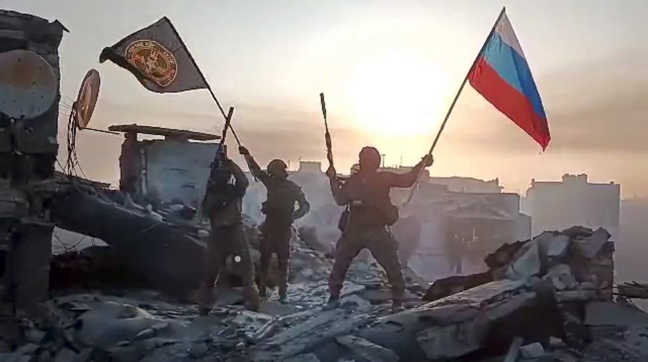 Leden van de Wagner Group van Yevgeny Prigozhin zwaaien met een Russische vlag en een Wagner-vlag boven op een beschadigd gebouw in Bachmoet. Het beeld komt uit een video die op 20 mei door Prigozhin Press Service is vrijgegeven.