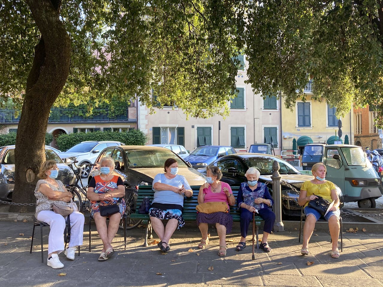 Bijeenkomst op een Italiaans dorpsplein op anderhalve meter afstand vanwege de coronacrisis. Zes dames dragen een mondkapje, verplicht op de meeste plekken in Italië.