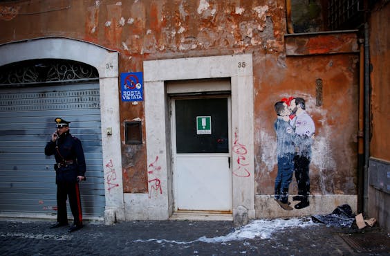 Een Italiaanse politieman houdt de wacht naast een muurschildering in Rome, waarop Lega-leider Matteo Salvini (r) en Luigi di Maio van de Vijfsterrenbeweging elkaar kussen.