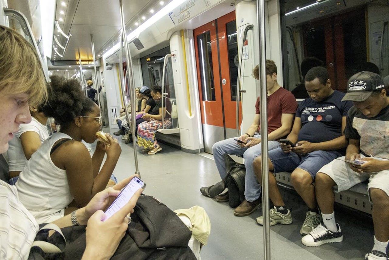 Passagiers in de metro van de Amsterdamse Noord-Zuidlijn kijken op hun telefoons.