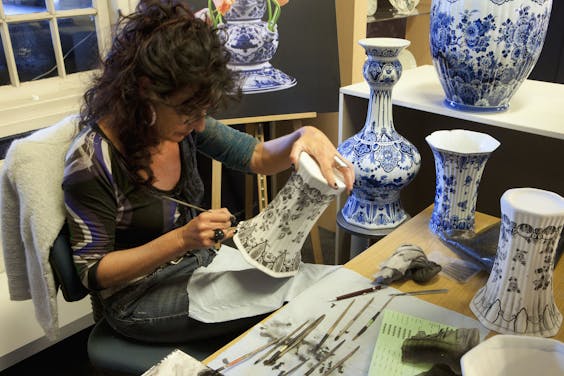 Een medewerker van de Koninklijke Porceleyne Fles beschildert een vaas.