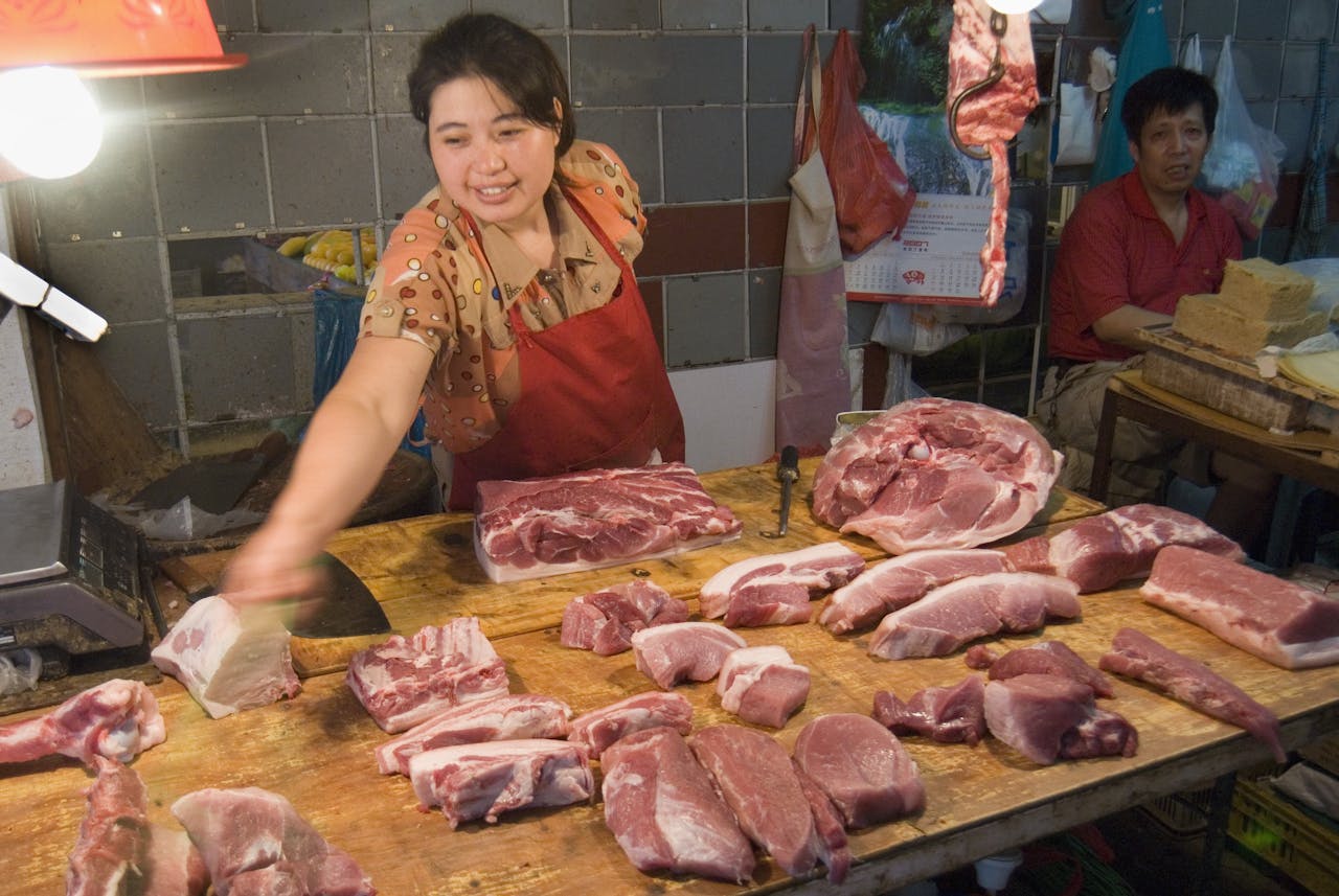 Een marktvrouw in Shanghai toont een keur aan varkensvlees, een belangrijke voedselbron voor veel Chinezen. Varkensvlees was in mei 3,2% goedkoper dan een jaar geleden.