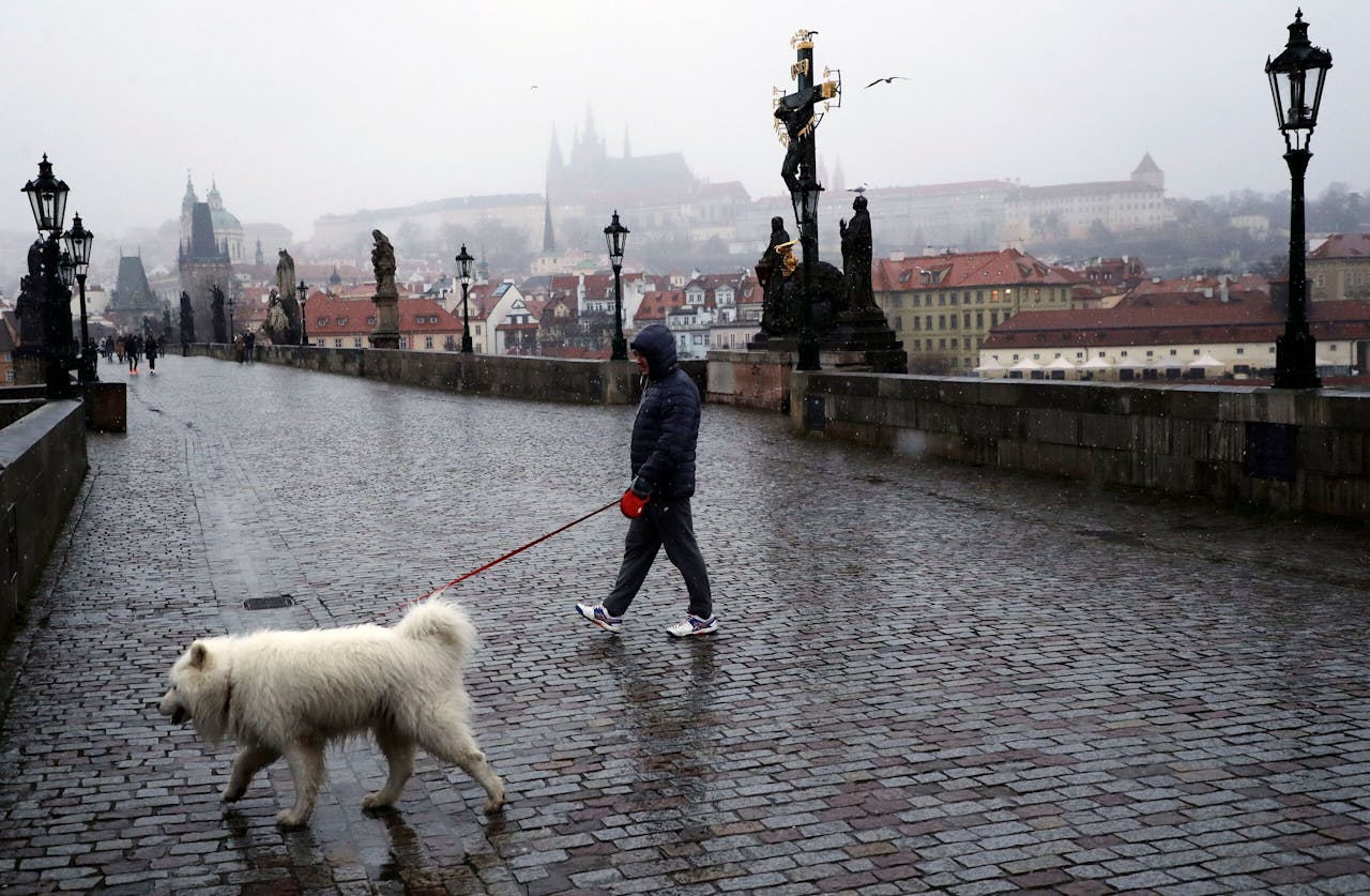Een man wandelt met zijn hond op de nagenoeg lege Karelsbrug in Praag. Net als in de rest van Europa zijn ook in Tsjechië winkels en horeca grotendeels dicht vanwege de coronapandemie.