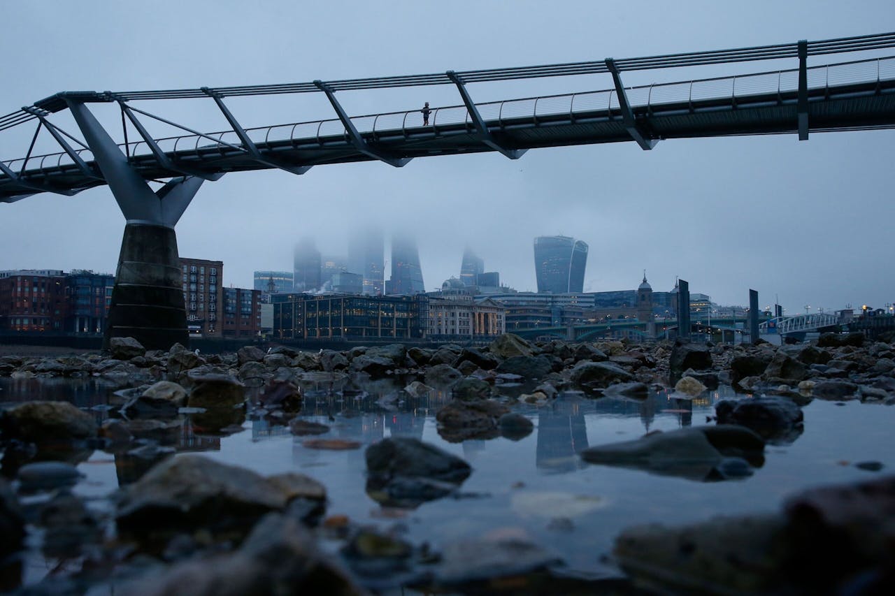 Een eenzame jogger op de Millennium Bridge tegen een achtergrond van de in mist gehulde kantoorgebouwen in the City, het financiële hart van Londen.