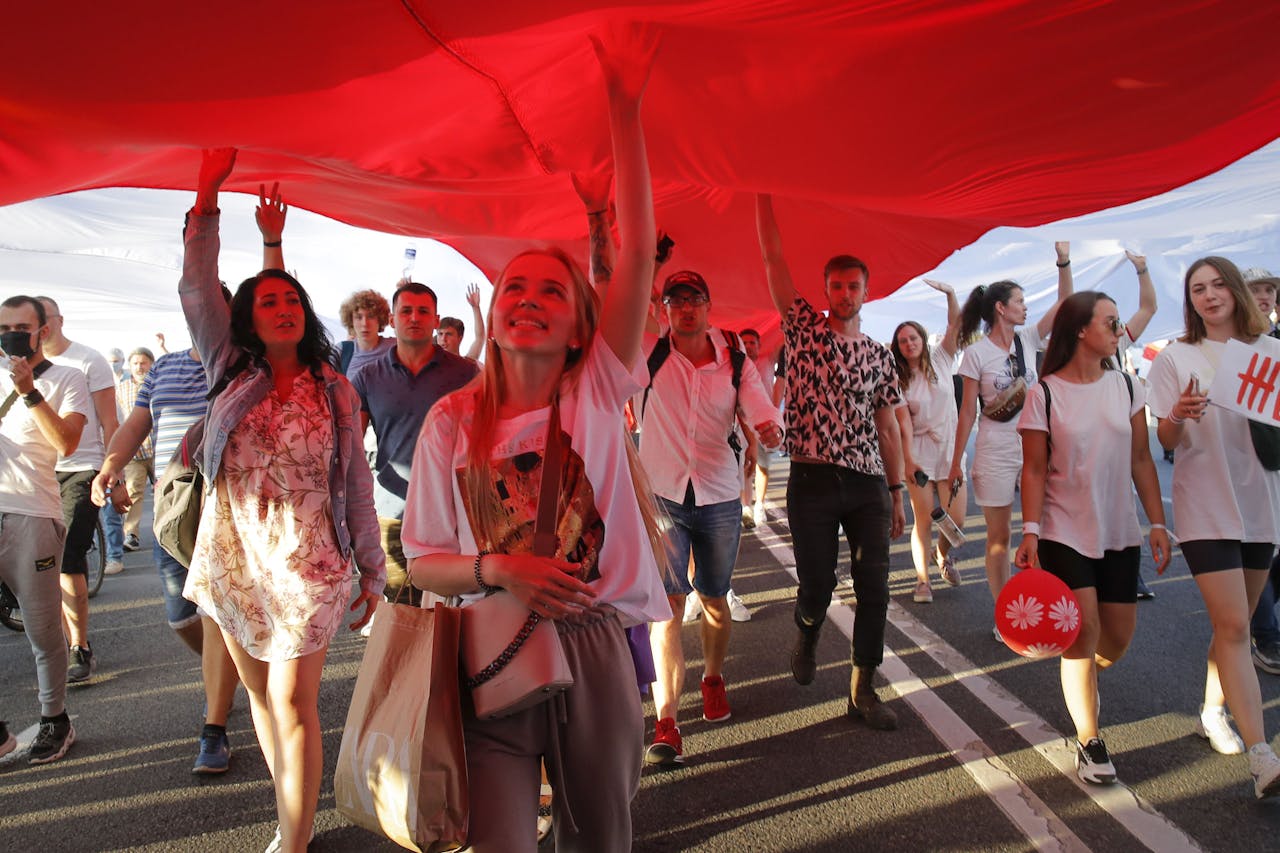Demonstranten droegen zondag een grote oud-Wit-Russische vlag door de straten van de hoofdstad Minsk. Zij demonstreerden met naar schatting tien- tot honderdduizenden anderen voor eerlijke, vrije verkiezingen in het land.