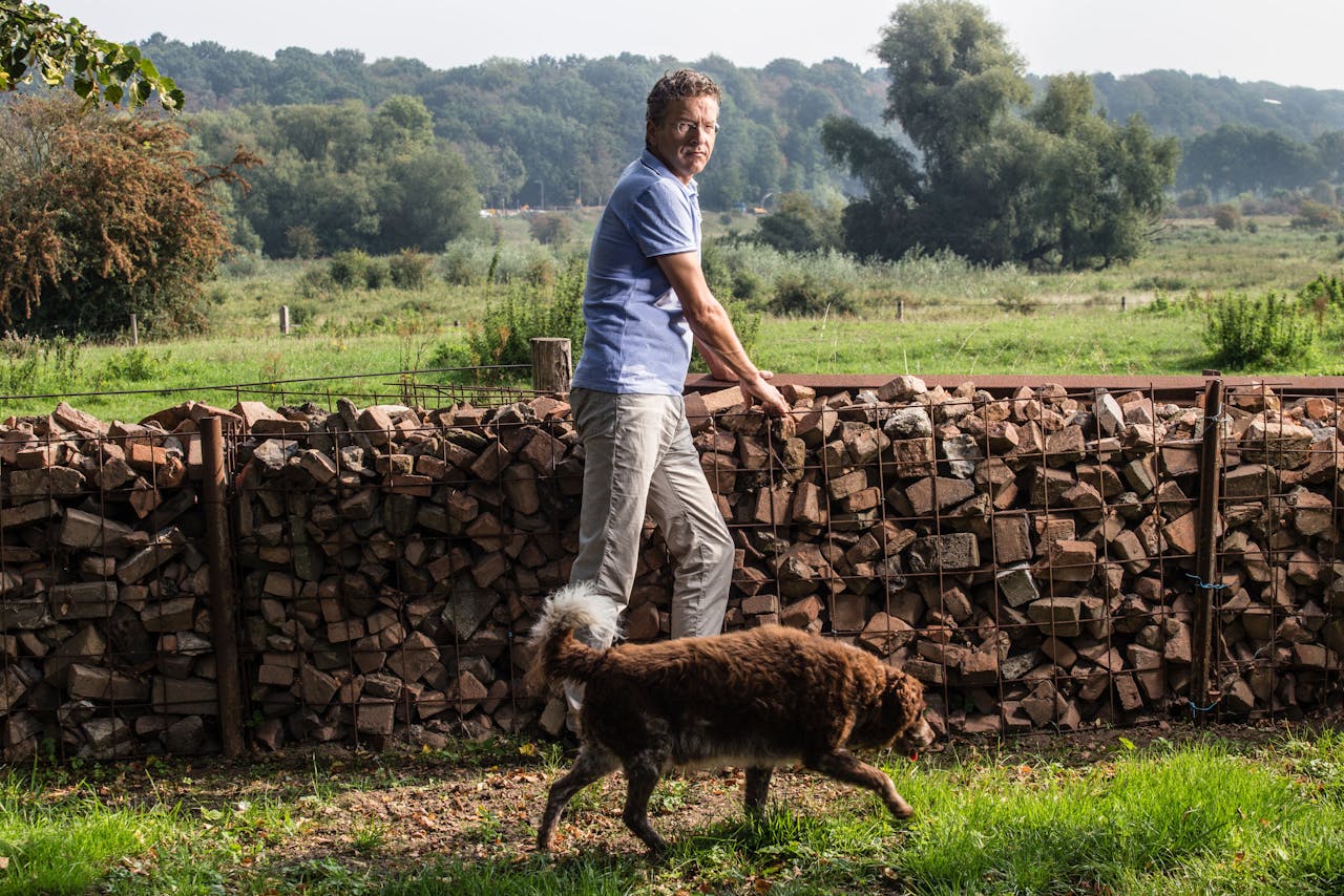 Jeroen Dijsselbloem (en zijn hond) bij een muur om zijn huis dat op een terp staat. De stenen komen van de oude gesloten steenfabrieken in de uiterwaarde.