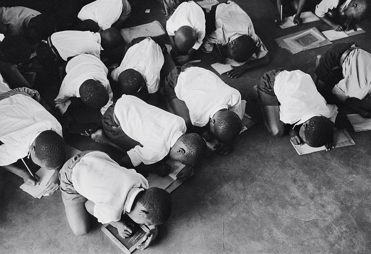 Zwarte schoolkinderen zitten op hun knieën tijdens schrijfles. Sinds 1953 was onderwijs in Zuid-Afrika gescheiden.
