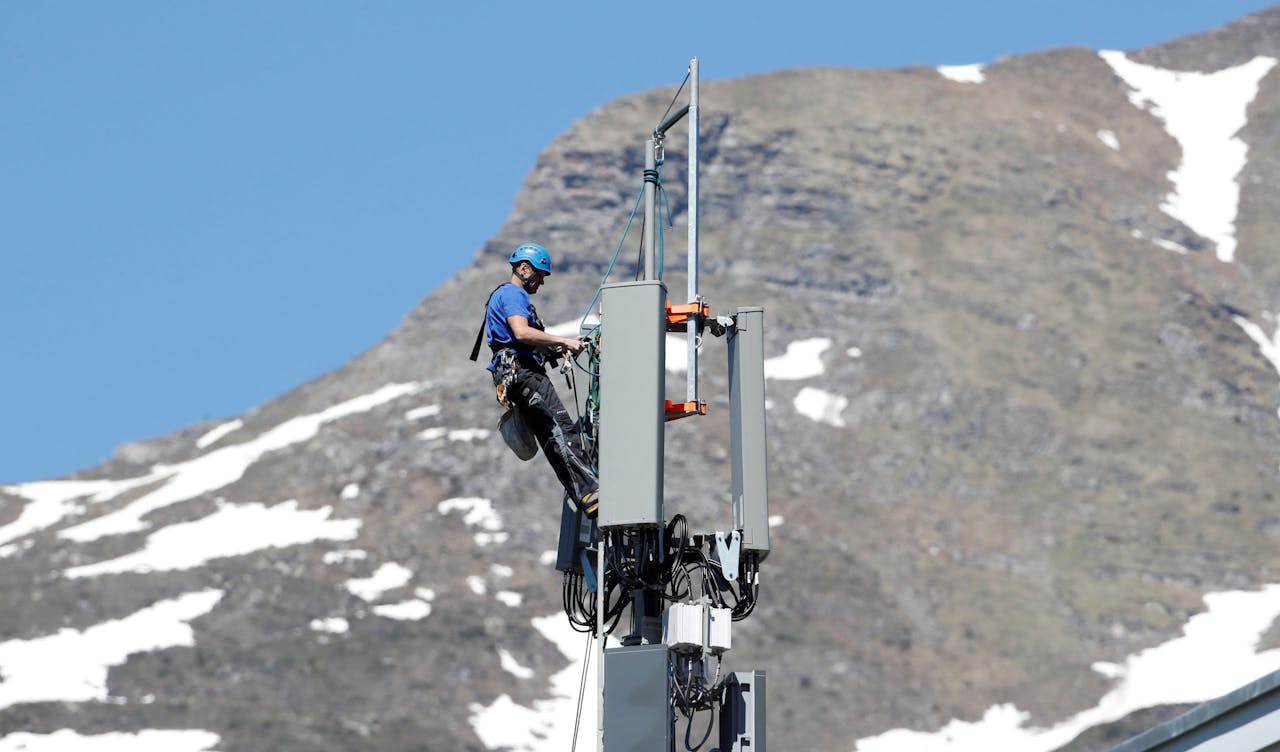 Een installateur, stevig vastgesnoerd bovenin de zendmast, is bezig met het plaatsen van een 5G antenne voor de Zwitserse telecomaanbieder Swisscom in het berggebied Lenzerheide.