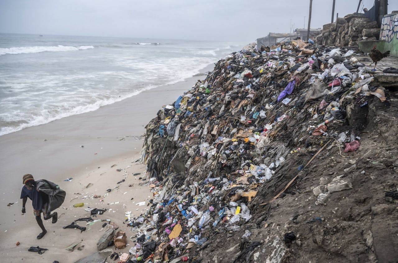 Een vuilnisraper loopt langs een berg aan textiel en ander afval bij Chorkor beach in Accra, Ghana. Ghana importeert iedere week 15 miljoen afgedankte kledingstukken, aldus de Amerikaans-Ghanese Or Foundation.