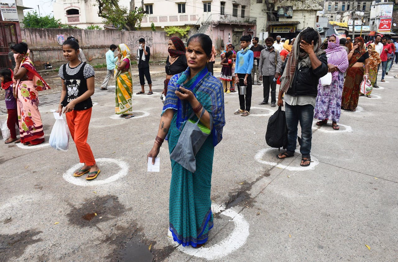 Daklozen en gestrande migrantenwerkers staan in New Delhi te wachten bij de uitdeling van voedselpakketten. In overeenstemming met de anticoronamaatregelen geven de cirkels op de grond een veilige afstand aan om besmetting te voorkomen.
