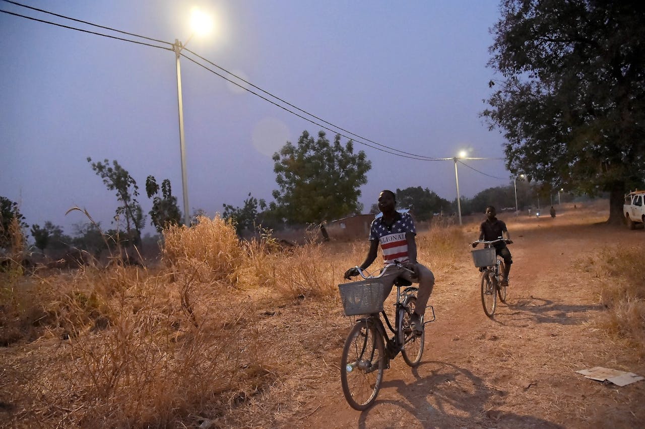 Fietsers rijden langs straatlantaarns op zonne-energie die vorig jaar februari werden geïnstalleerd in het dorp Takpapieni, in het noorden van Togo.