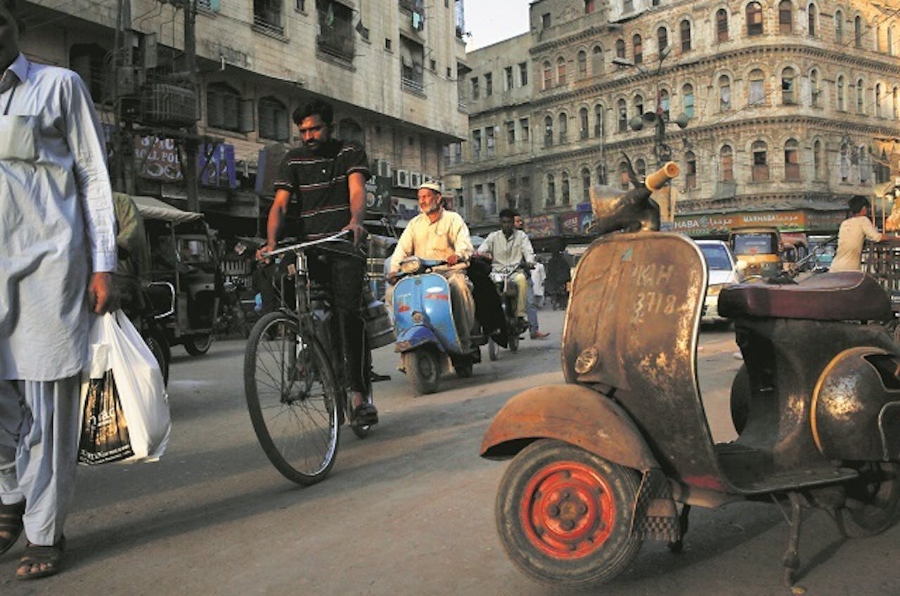 De blauwe Vespa-scooter in het verkeer in Karachi zag er ooit zo uit als het roestige exemplaar op de voorgrond.