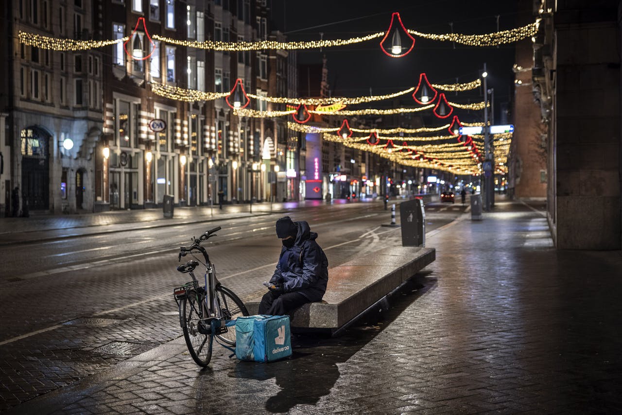 Een maaltijdbezorger wacht - onbetaald- op orders bij de KFC en McDonalds op het lege Damrak in Amsterdam.