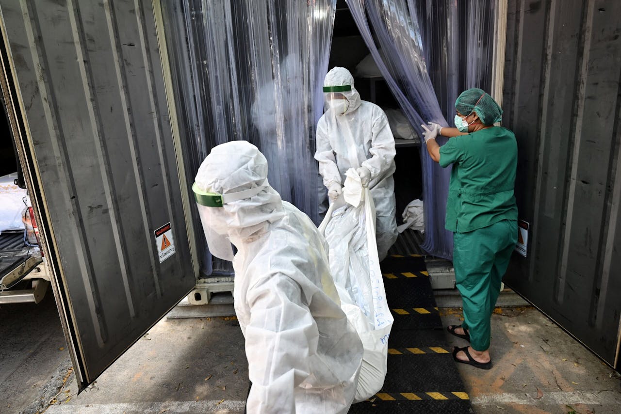 Ziekenhuismedewerkers dragen een covidslachtoffer uit het mortuarium van het Thammasat ziekenhuis juist ten noorden van Bangkok. Thailand noteerde woensdag een nieuw record met ruim 20.000 nieuwe besmettingen in 24 uur.