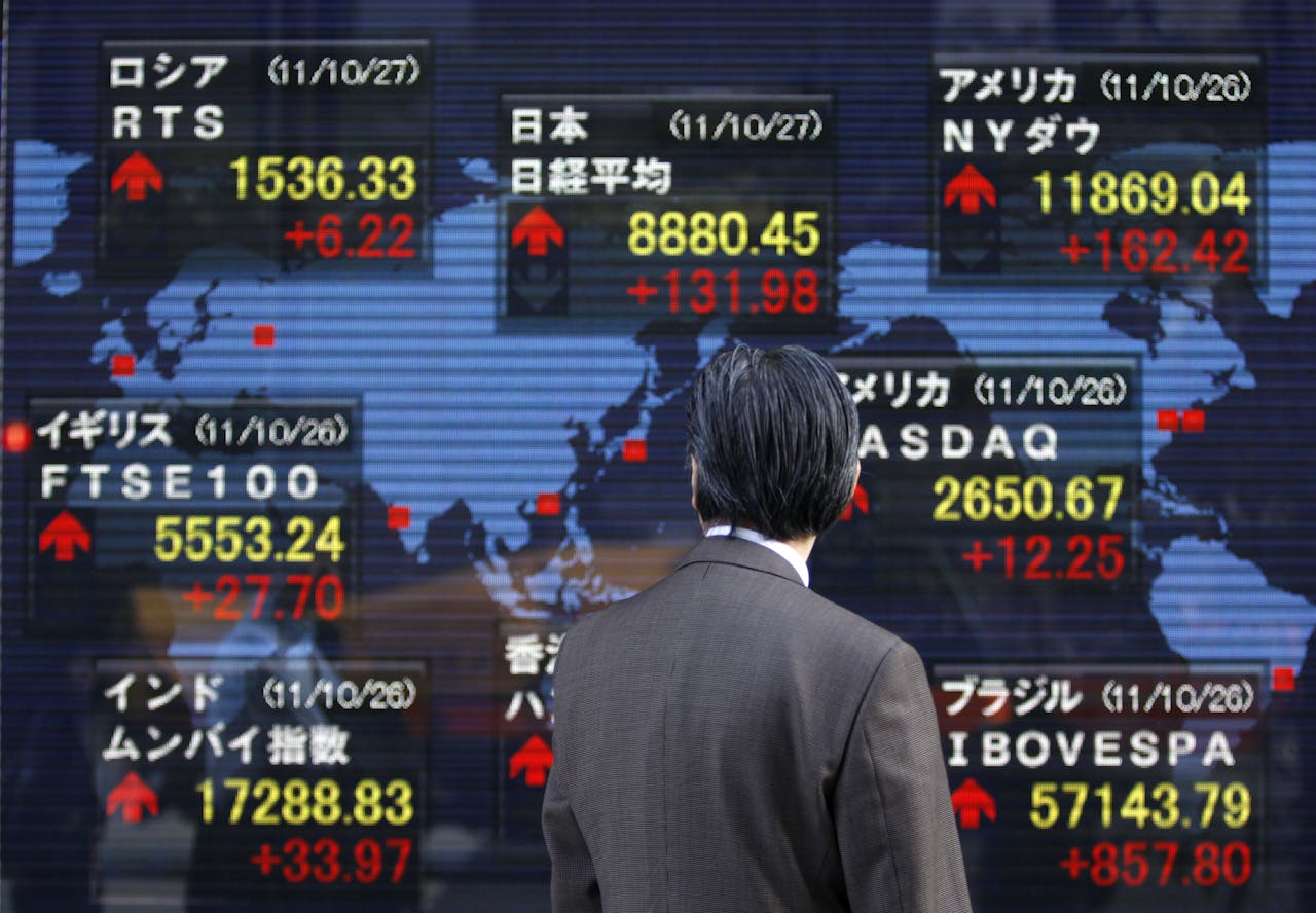 Een man kijkt naar de ontwikkeling van de koersen op schermen bij een beurshandelaar in Tokio. Beurzen in Azië reageerden positief op het akkoord dat in Brussel was bereikt. De Nikkei sloot 2,04% hoger.
