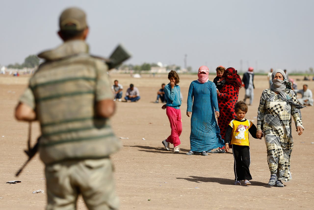 Een Turkse soldaat kijkt toe hoe Koerdisch-Syrische vluchtelingen langs de grens wandelen bij het Syrische grens stadje Kobani.