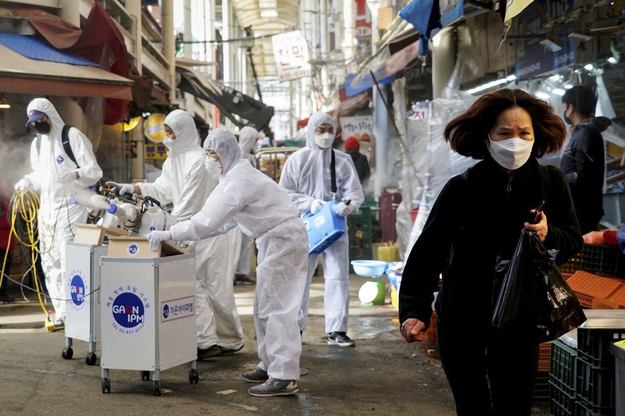 Een vrouw met een mondmasker loopt over een markt in Seoul, Zuid Korea, terwijl deze gedesinfecteerd wordt. De plotselinge stijging van besmettingen in landen als Italië, Iran en Zuid-Korea baart de Wereldgezondheidsorganisatie (WHO) zorgen.