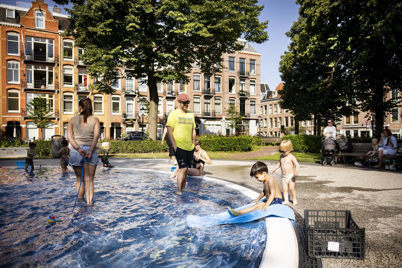Amsterdammers zoeken de verkoeling op bij een fontein op het Bellamyplein.