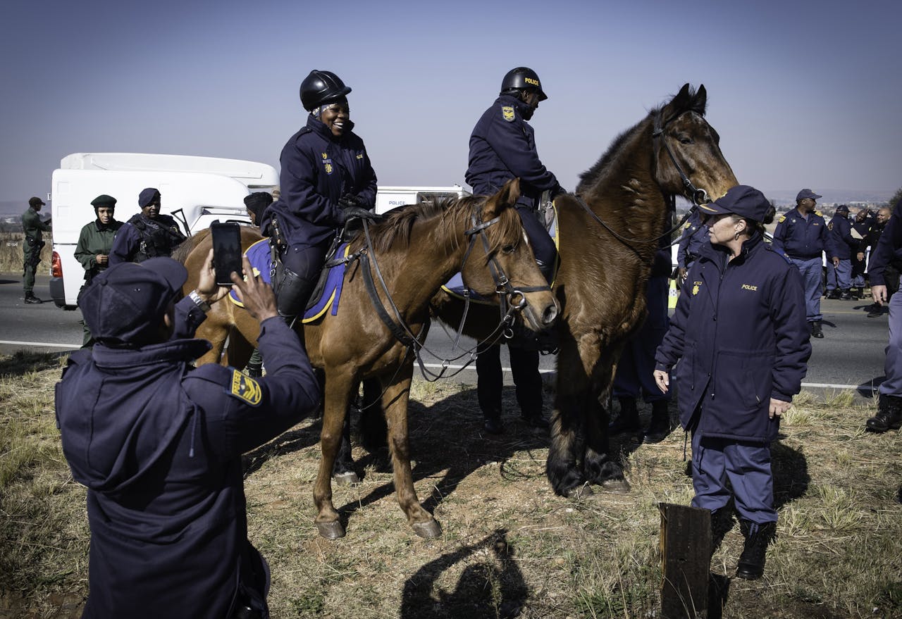 Een politieagent neemt een foto van een collega te paard tijdens een wegblokkade op de N12 bij Lenasia, een wijk buiten Johannesburg.