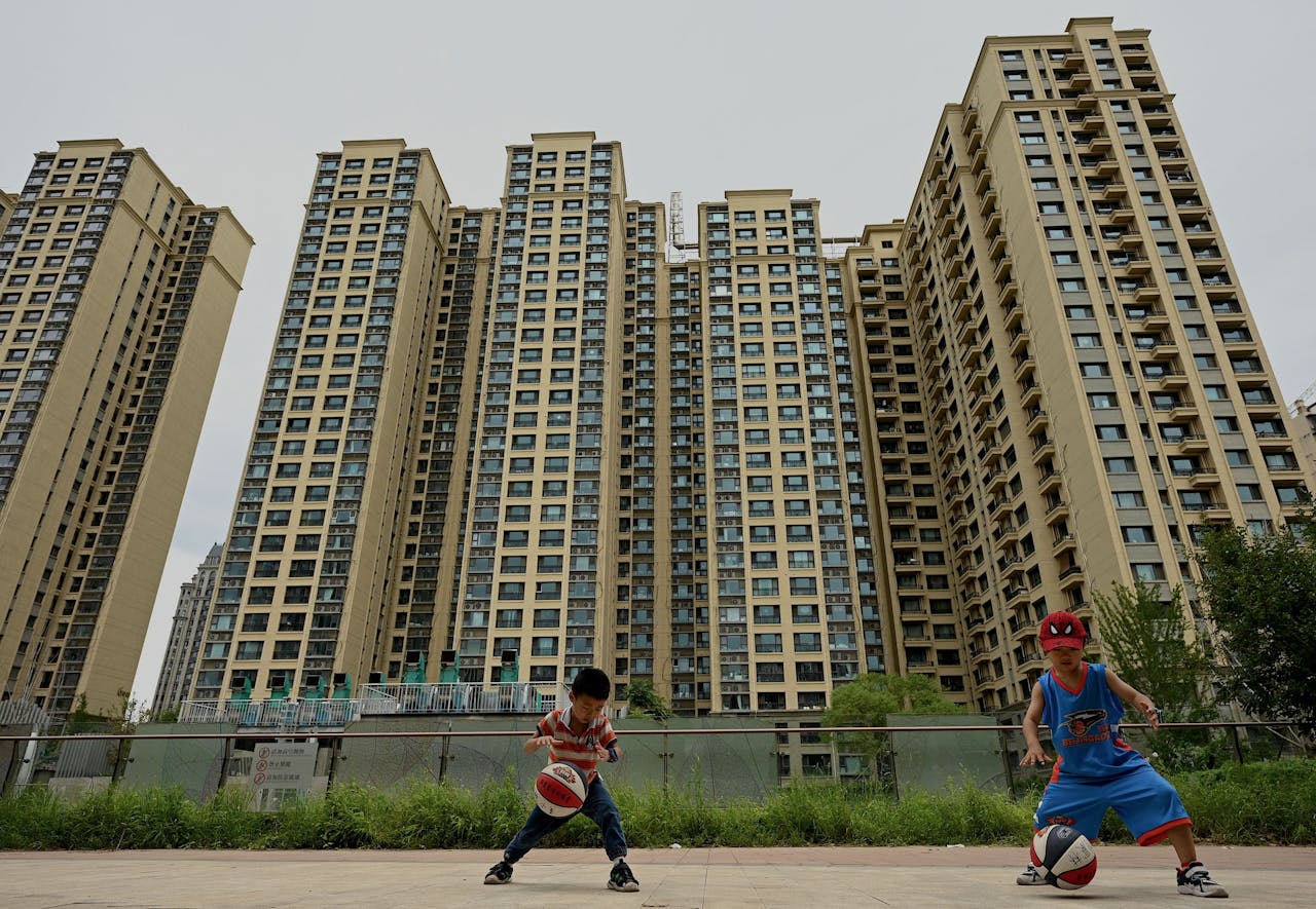 Kinderen spelen basketbal nabij een woontorencomplex in Peking van de Chinese vastgoedontwikkelaar Evergrande, dat vorig jaar in acute financiële problemen raakte.