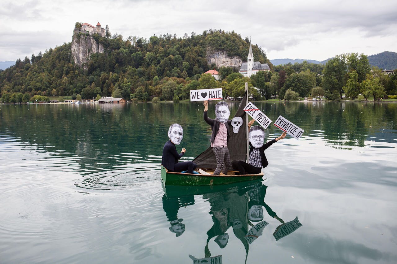 Demonstranten in een bootje op het meer van Bled in Slovenië dragen maskers van de Sloveense premier Janez Jansa, de Hongaarse premier Viktor Orbán en de Servische president Aleksandar Vucic. Ze protesteren tegen de aantasting van persvrijheid.