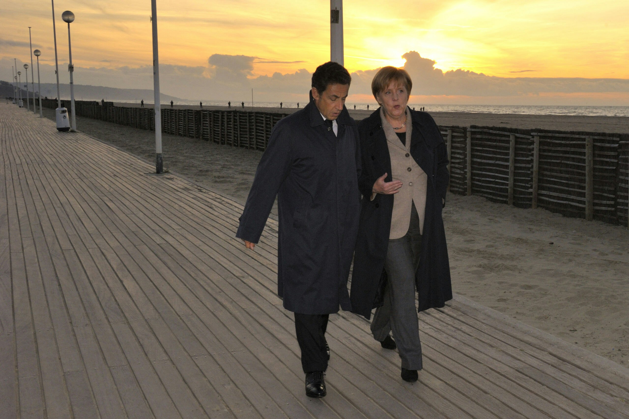 Tijdens een strandwandeling besluiten Nicolas Sarkozy en Angela Merkel dat banken voortaan moeten meebetalen aan de redding van eurolanden.