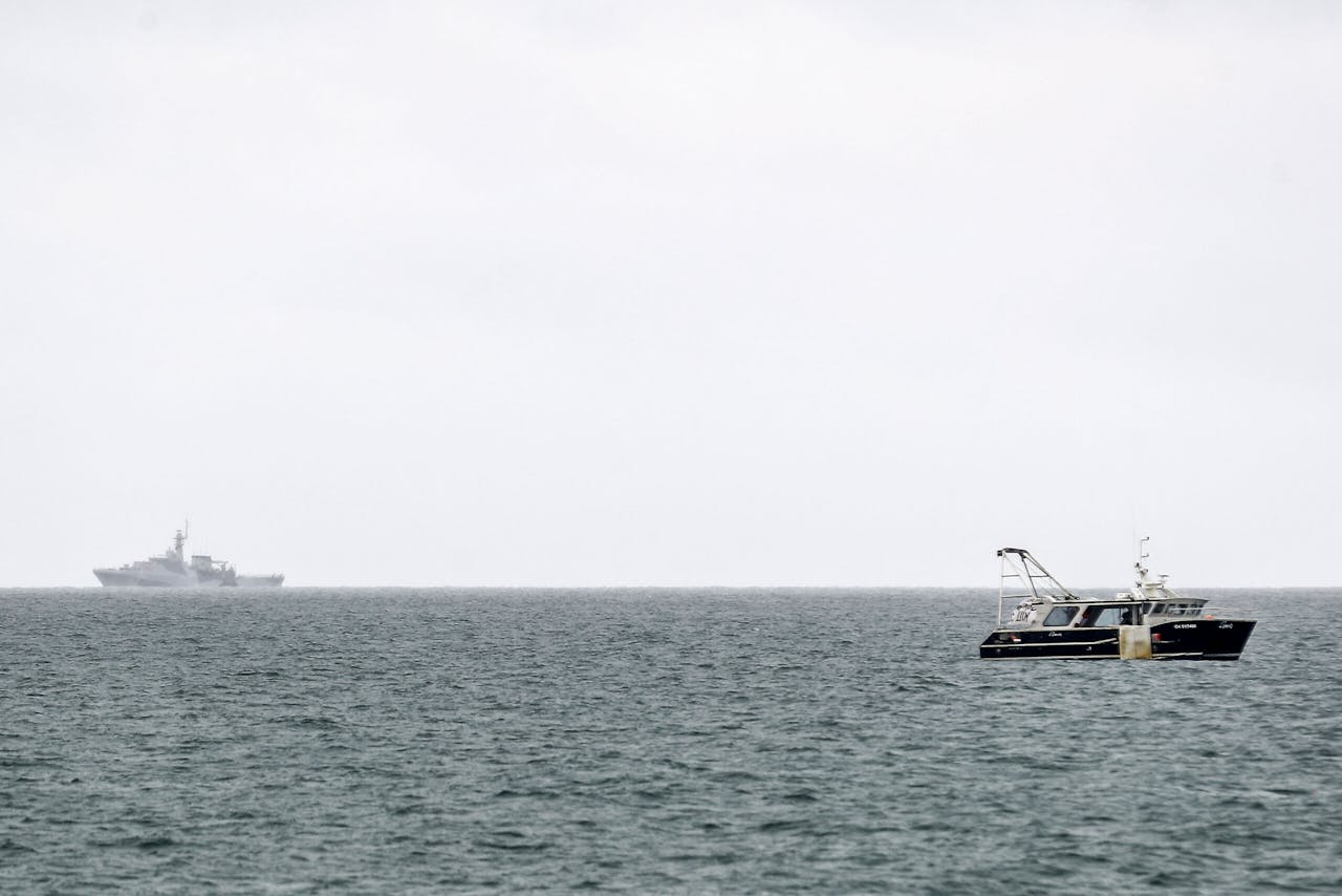 Een vissersboot met op de achtergrond een patrouilleschip van de Britse marine bij Jersey.