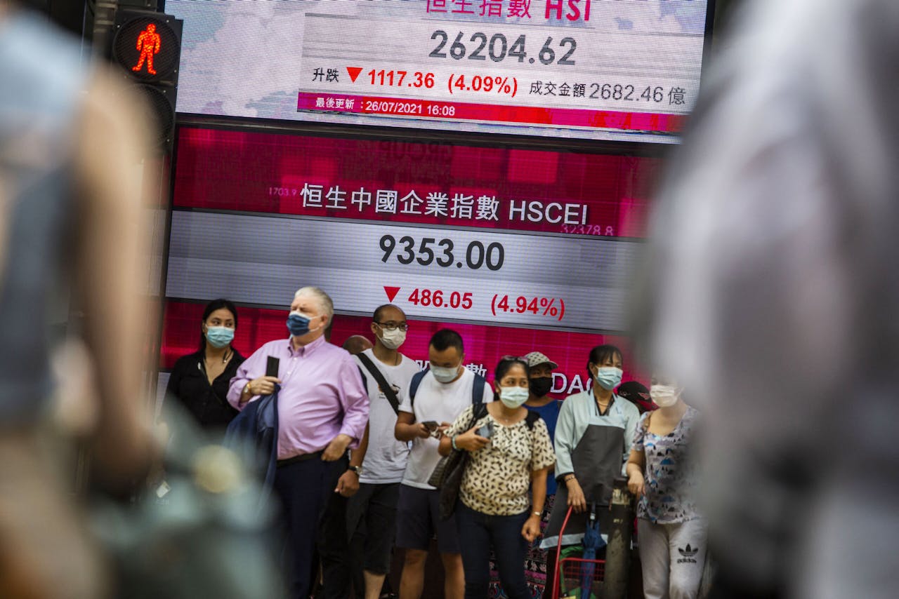People stand in front of an electronic display showing the Hang Seng Index in the Central district of Hong Kong on July 26, 2021, after stocks plunged as tuition firms were hammered by China's decision to reform the private education sector by preventing them from making profits. ISAAC LAWRENCE / AFP