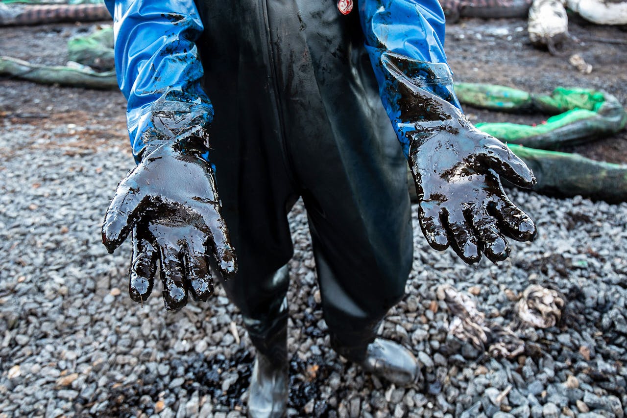 Een vrijwilliger laat zijn armen zien die bedekt zijn met olie, gelekt uit een bulkschip die in juli vorig jaar voor de kust van Mauritius strandde.
