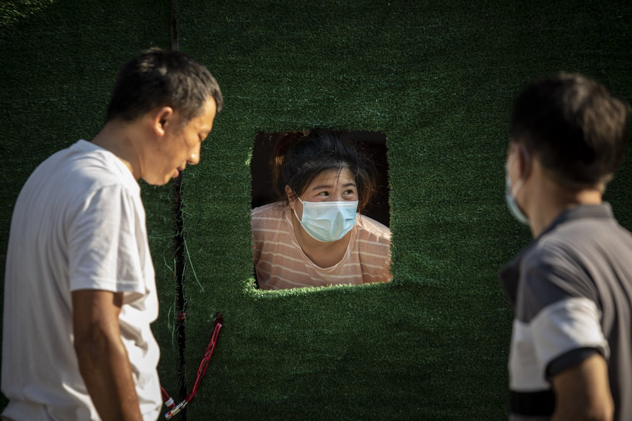 Een inwoner in Shanghai praat door een luik van een wijk die weer afgegrendeld is wegens een covidgeval.