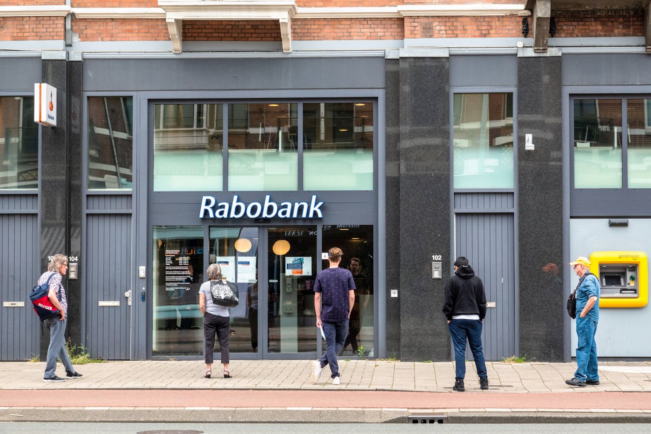 Klanten van Rabobank wachten tot het filiaal in de Amsterdamse Van Baerlestraat de deuren opent.