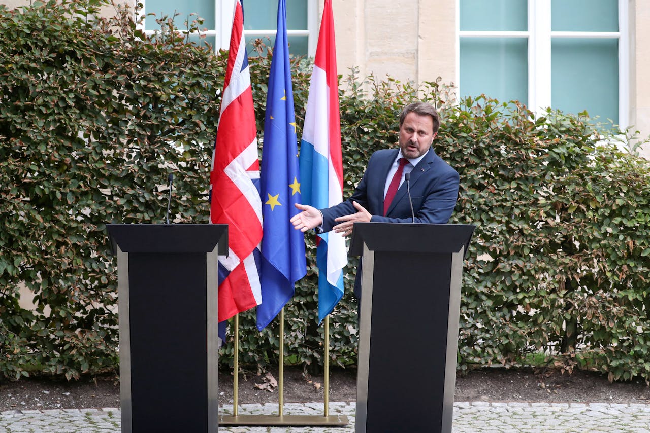 Waar is Boris Johnson? De Luxemburgse minister-president Xavier Bettel wijst tijdens een persconferentie naar de plaats waar zijn Britse ambtsgenoot had moeten staan.