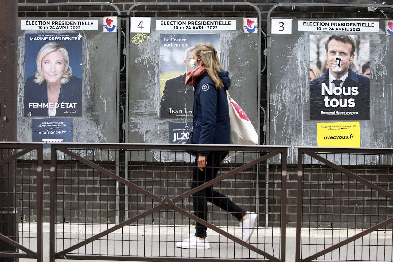 Een Parijse vrouw loopt langs verkiezingsplakkaten van Marine Le Pen (links) en Emmanuel Macron (rechts).