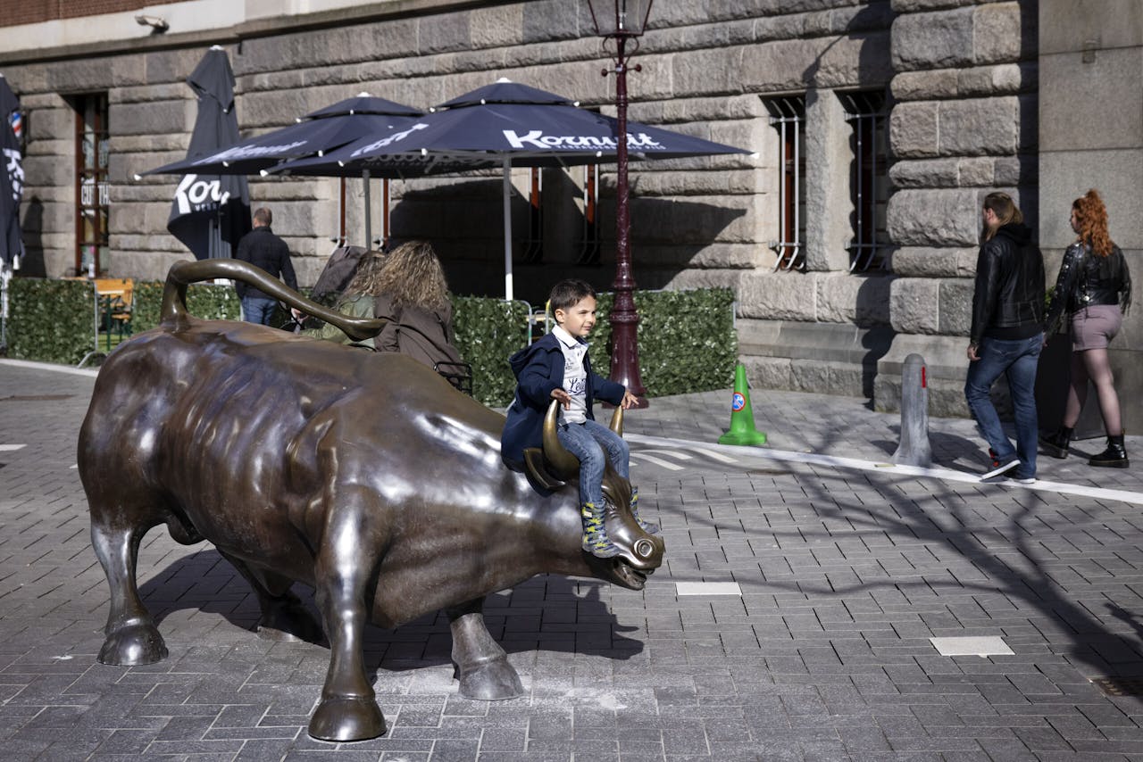 Een kind poseert op het beeld van de stier op Beursplein 5 in Amsterdam. De stier symboliseert stijgende koersen op de financiële markten.